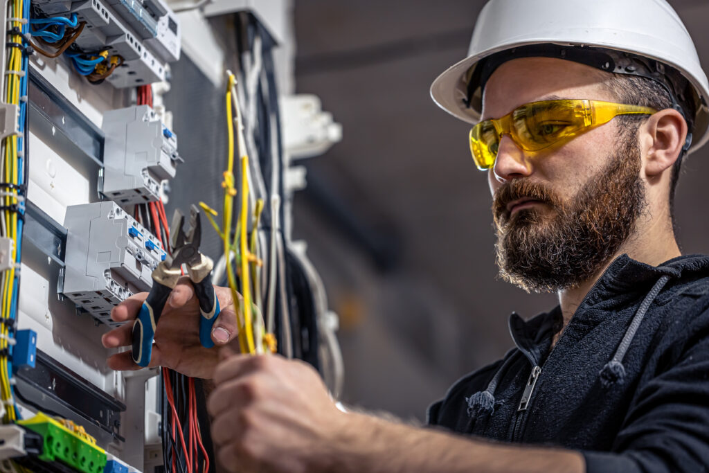 Villanyszerelő elektromos vezetéket köt be a kapcsolószekrényben